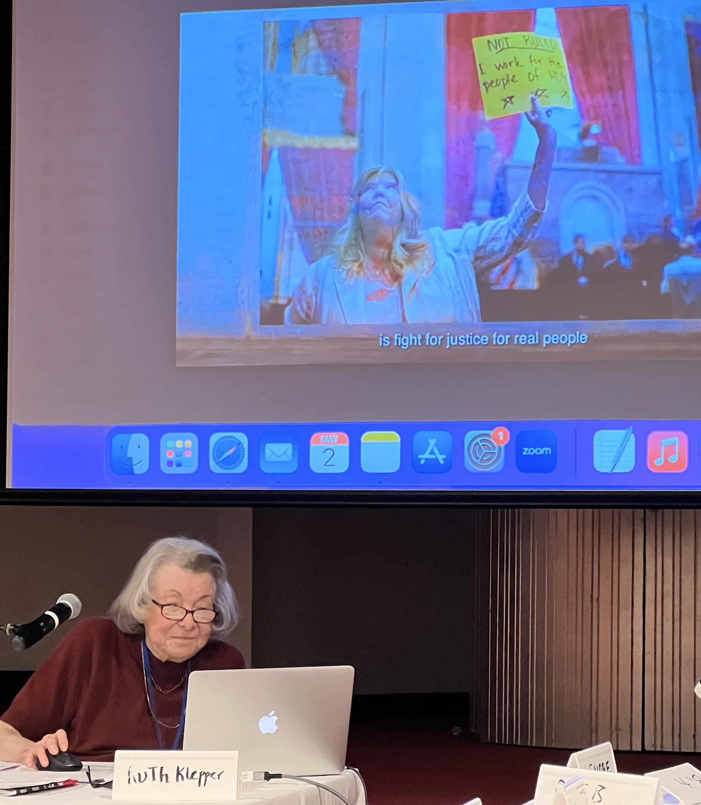 Ruth Klepper teaching a class on Democracy with a colorful slide projected behind her